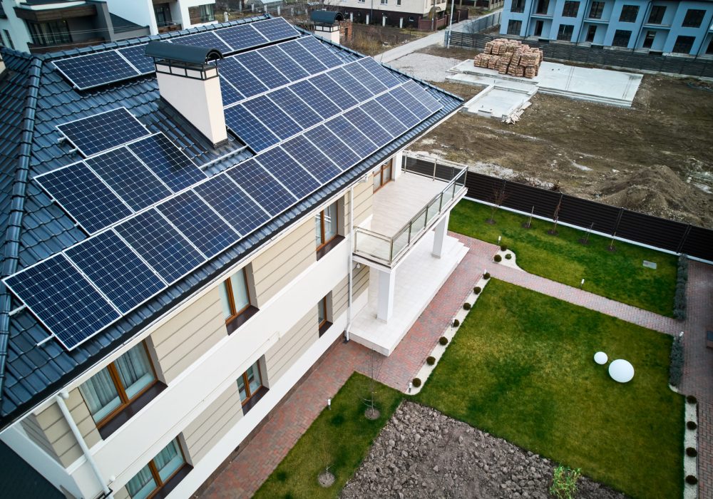 Residential house with photovoltaic solar panel modules on rooftop and green grass on backyard. Home with solar electric system, lawn and pavement outside. Renewable energy and housing concept.